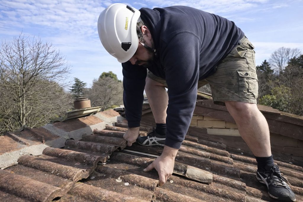 roofer lifting a broken roof tile to repair a leak